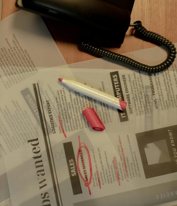 Close-up of a job search scene with a newspaper, red marker, and telephone, indicating job hunting.